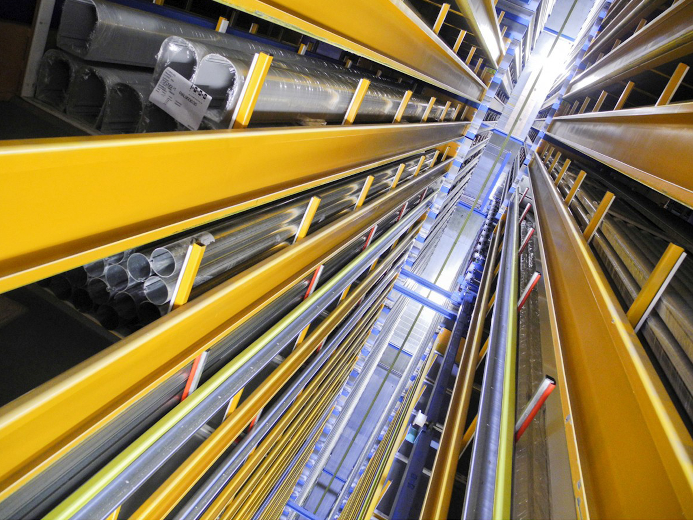 A view of the yellow-painted aisles of a high-bay warehouse where long goods (tubes, etc.) are stored
