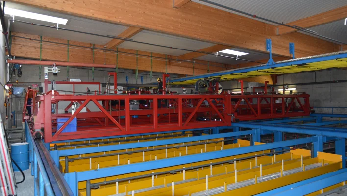 View from above, looking down on the aisles of the high-bay warehouse and the top crossbeam of a storage/retrieval system, steel structure in red, blue and yellow