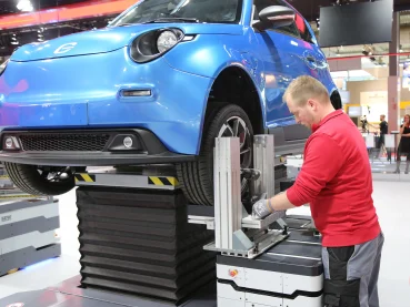 Blaues e.GO-Fahrzeug / Werker mit rotem Pullover montiert ein Rad